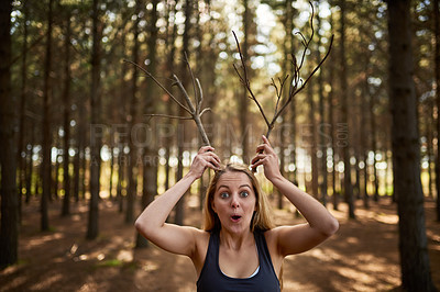 Buy stock photo Portrait of a playful young woman holding tree branches up like antlers in the forest