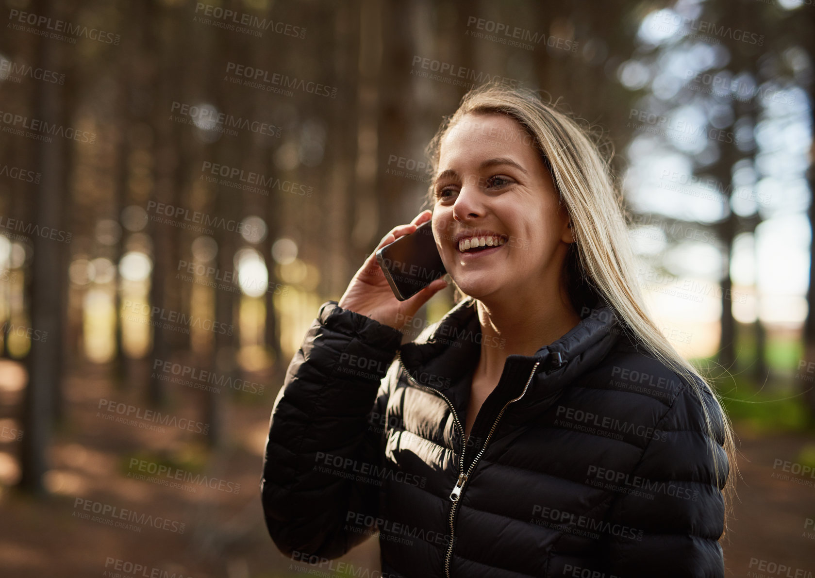 Buy stock photo Shot of a happy young woman talking on her cellphone while walking in the forest