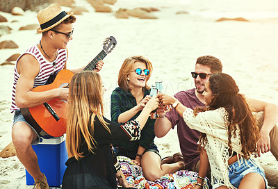 Buy stock photo Shot of a young man playing guitar for his friends while chilling on the beach