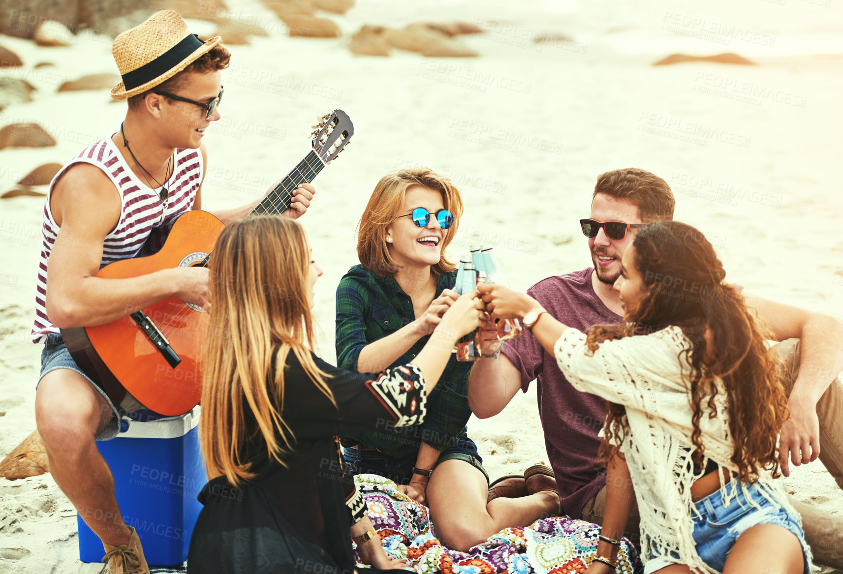 Buy stock photo Shot of a young man playing guitar for his friends while chilling on the beach