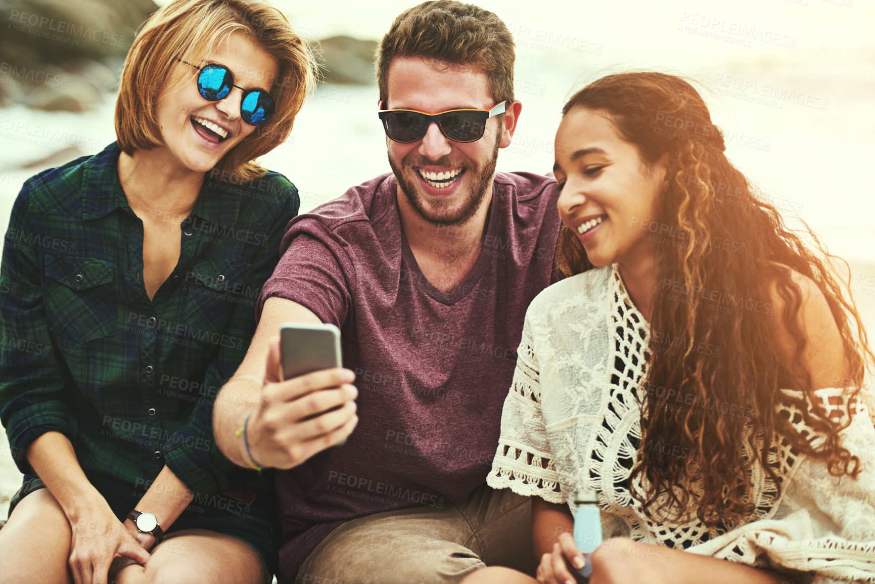 Buy stock photo Cropped shot of a young man showing two female friends something on his cellphone