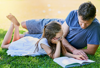 Buy stock photo Shot of a father and his little daughter reading a book together on the grass outside