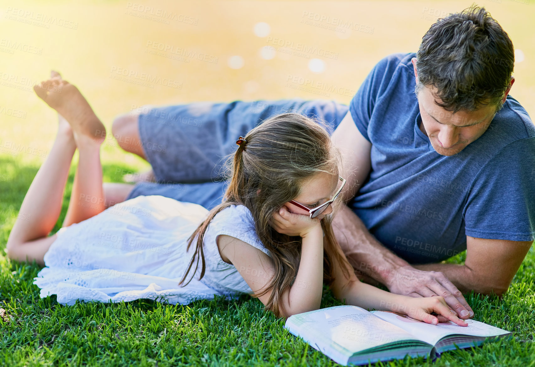 Buy stock photo Shot of a father and his little daughter reading a book together on the grass outside