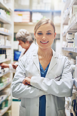 Buy stock photo Portrait of a pharmacist standing in a isle with her colleague working in the background