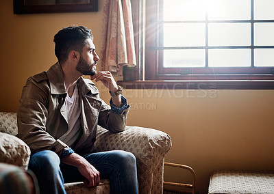 Buy stock photo Shot of a handsome young man deep in thought while sitting on a chair at home