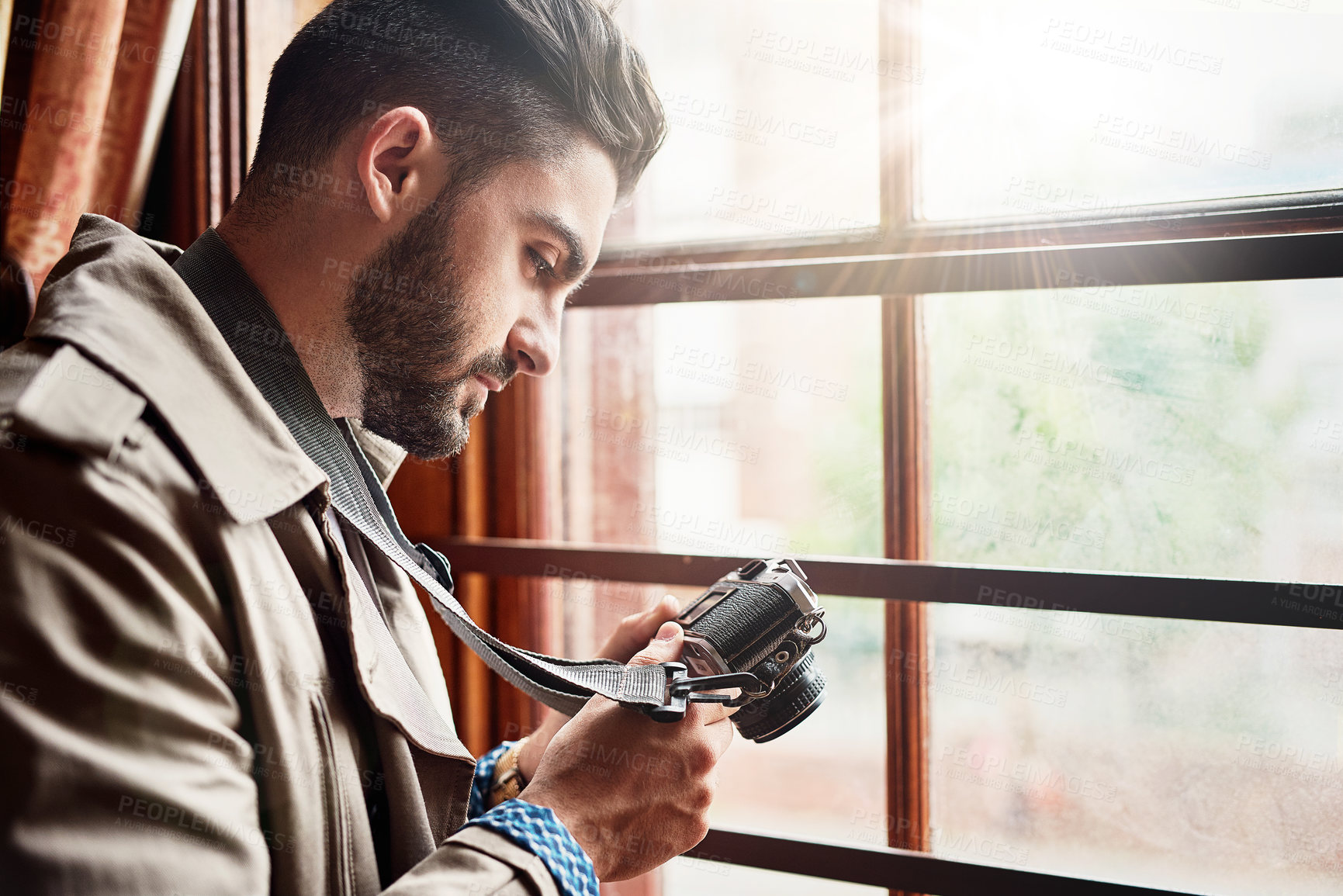 Buy stock photo Shot of a handsome young man standing by a window at home looking at his camera