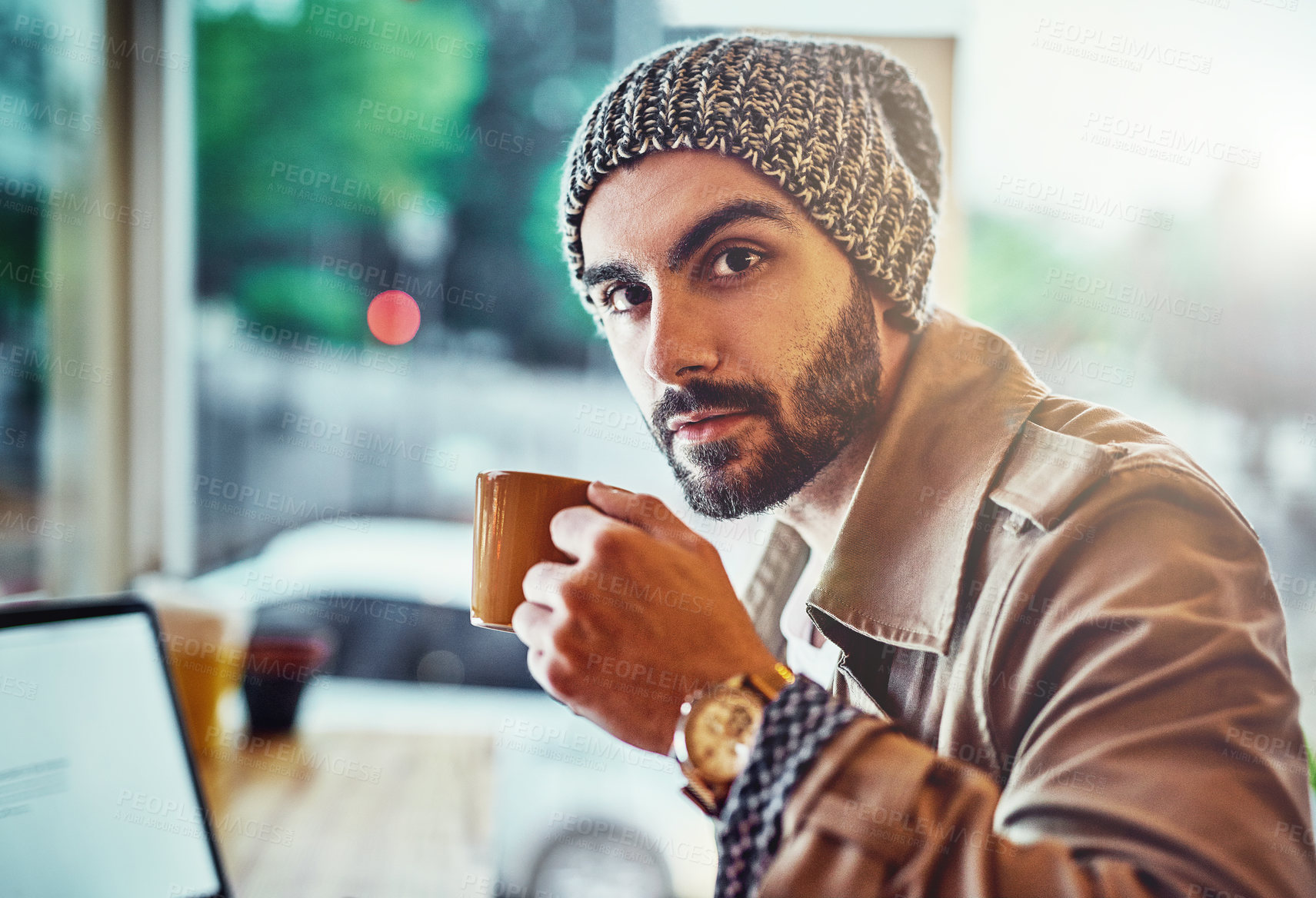 Buy stock photo Portrait of a handsome young man sitting at a cafe counter using a laptop and drinking a cup of coffee