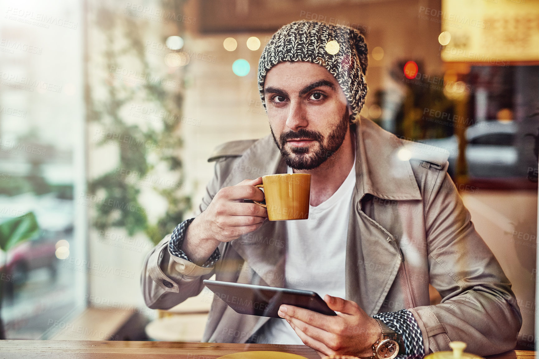 Buy stock photo Portrait of handsome young man drinking a coffee and using a digital tablet while sitting at a counter in a cafe