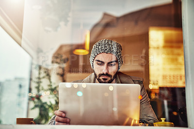 Buy stock photo Shot of a handsome young man sitting at a cafe counter using a laptop