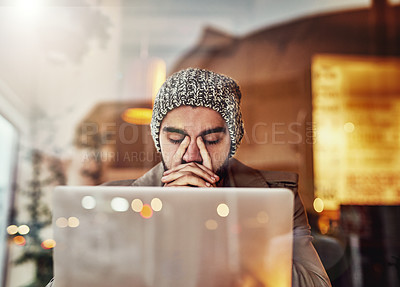 Buy stock photo Shot of a young man looking stressed while using a laptop in a cafe