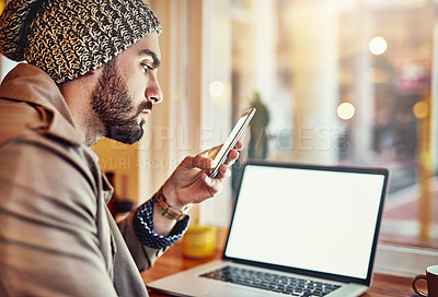 Buy stock photo Shot of a stylish young man reading a text message and using a laptop while sitting in a cafe