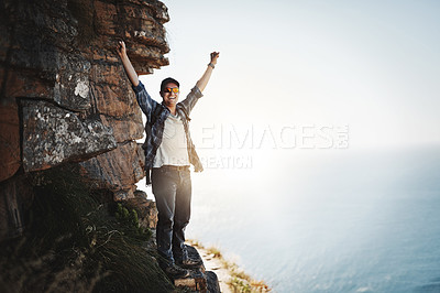 Buy stock photo Portrait of a young man standing on a mountain cliff with his arms raised