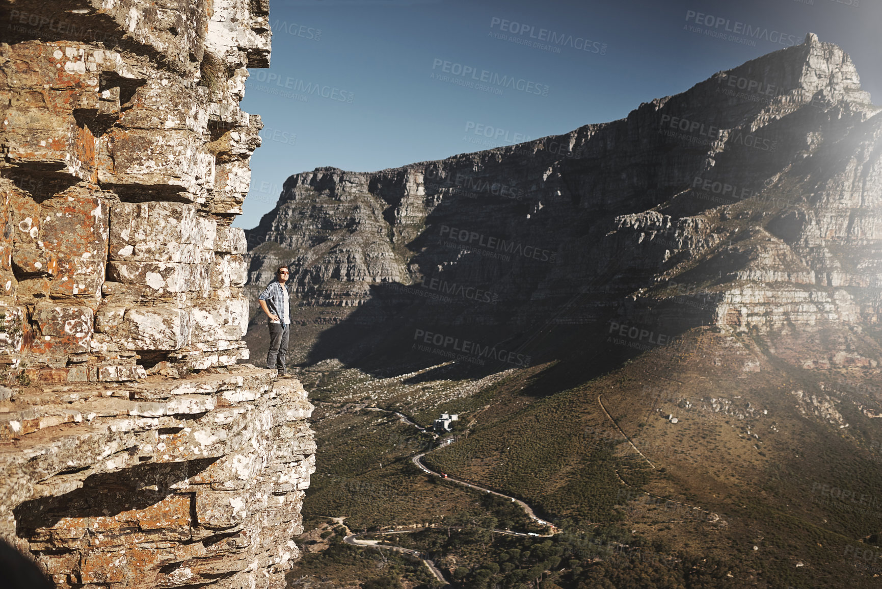 Buy stock photo Shot of a young man standing on the edge of a mountain cliff overlooking a valley