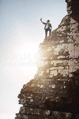 Buy stock photo Shot of a young man taking photographs while standing on the edge of a mountain cliff