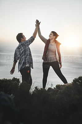 Buy stock photo Shot of a young couple high fiving after making it to the top of the mountain