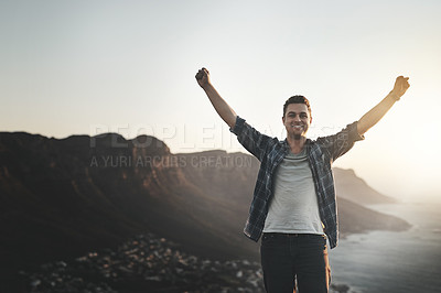Buy stock photo Portrait of a young man standing on a mountain cliff with his arms raised