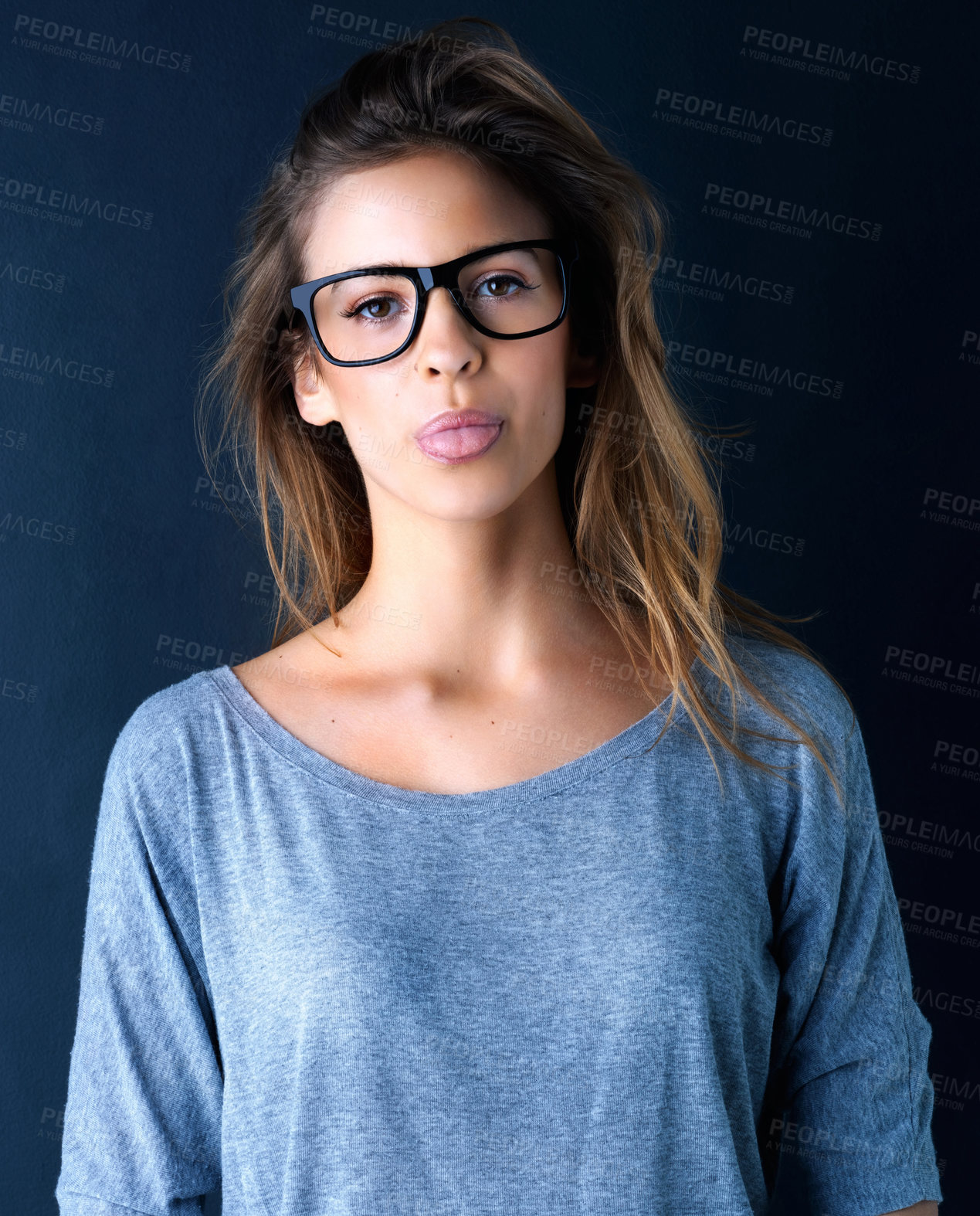 Buy stock photo Studio portrait of a cute teenage girl in glasses sticking out her tongue posing against a dark background