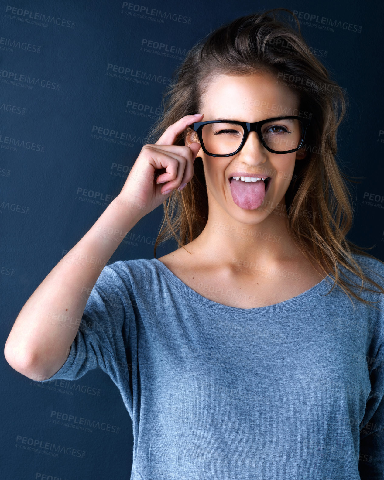 Buy stock photo Studio portrait of a cute teenage girl in glasses sticking out her tongue posing against a dark background