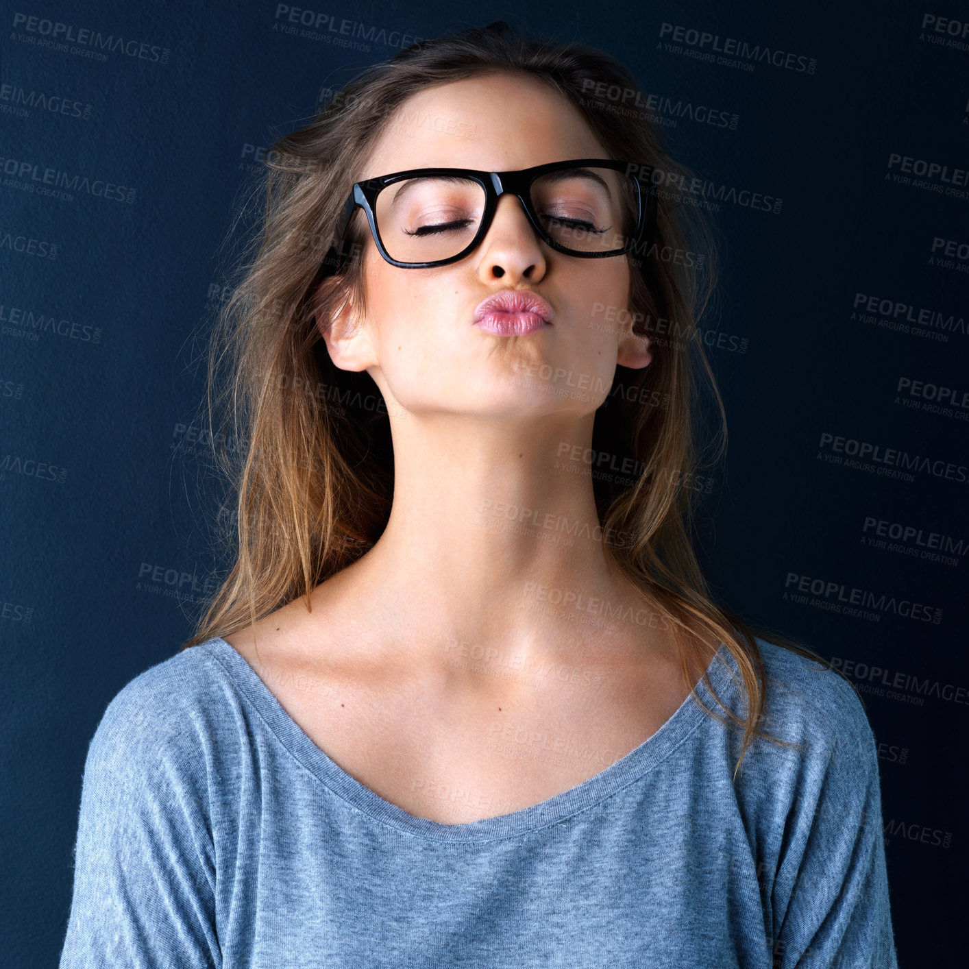 Buy stock photo Studio shot of a cute teenage girl in glasses blowing a kiss posing against a dark background