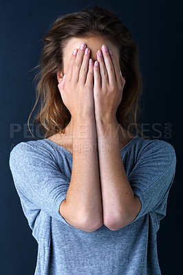 Buy stock photo Studio shot of a teenage girl with her hands covering her eyes against a dark background