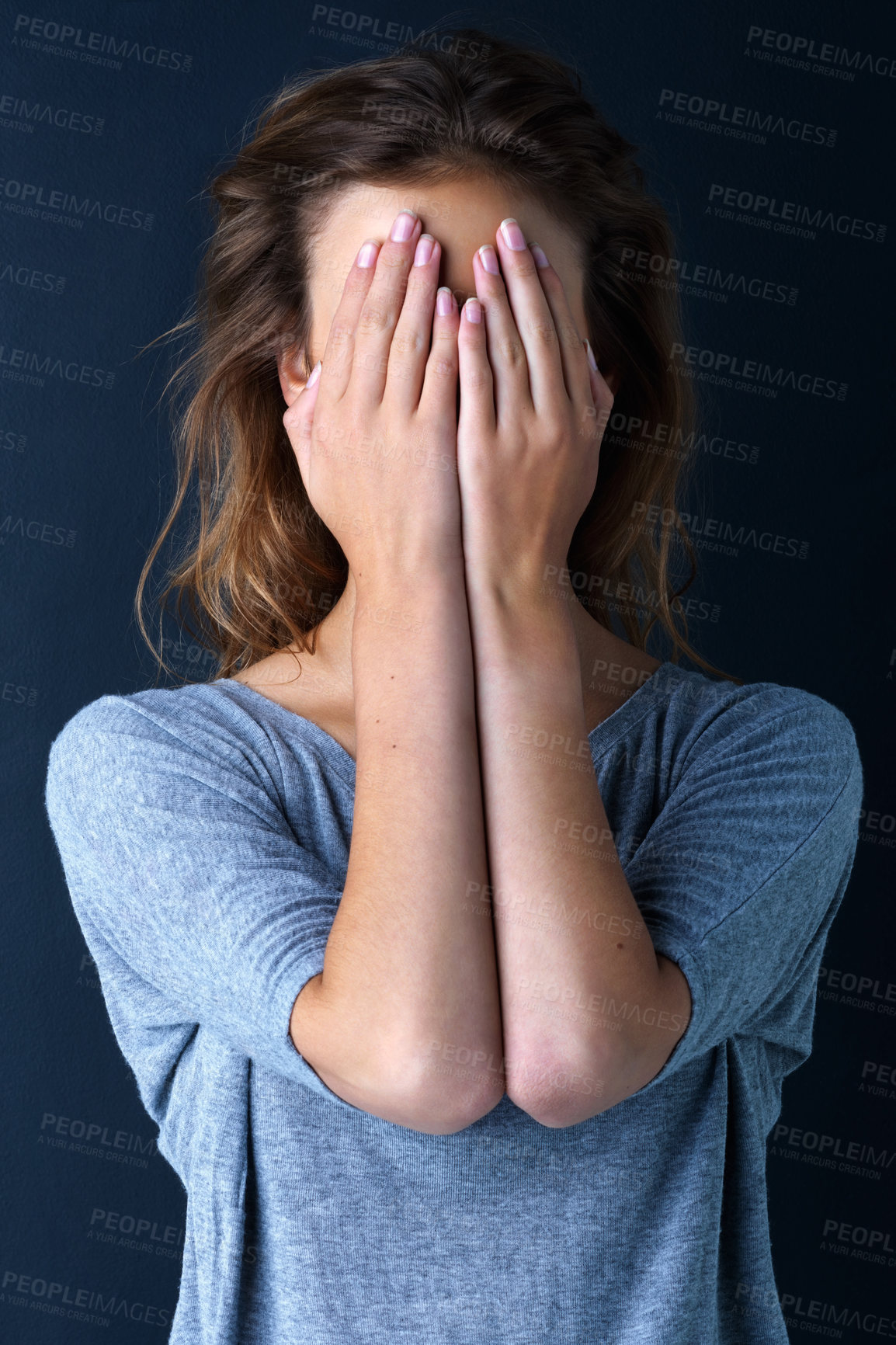 Buy stock photo Studio shot of a teenage girl with her hands covering her eyes against a dark background