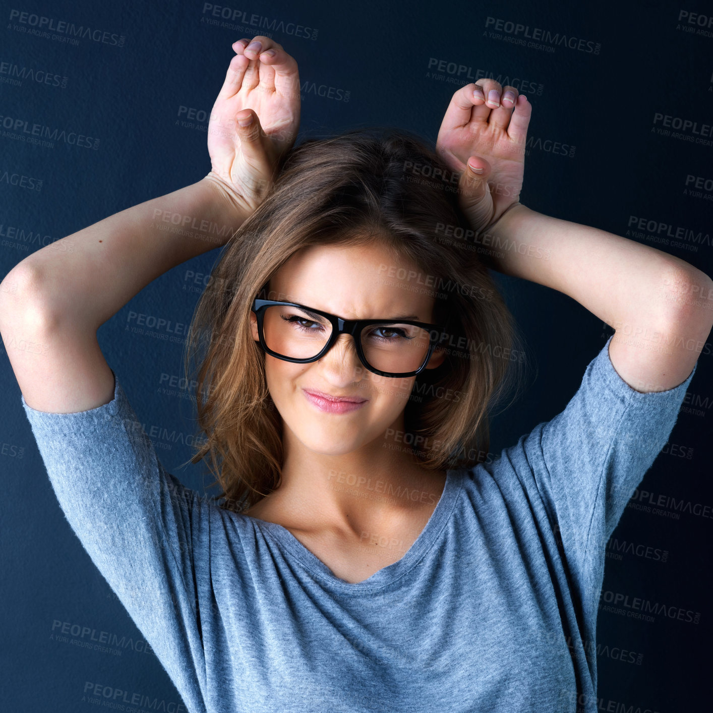 Buy stock photo Studio portrait of a teenage girl playfully making ears with her hands against a dark background
