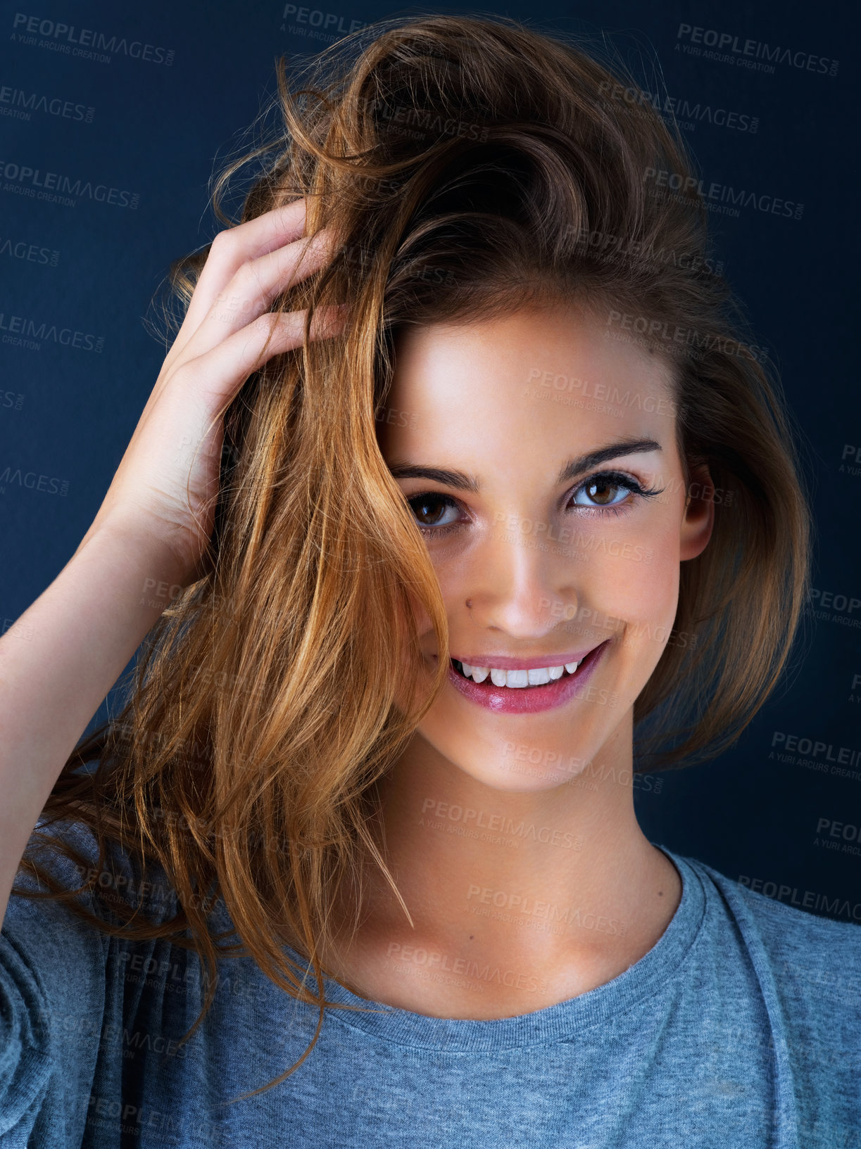 Buy stock photo Studio portrait of a cute teenage girl with her hand in her hair posing against a dark background