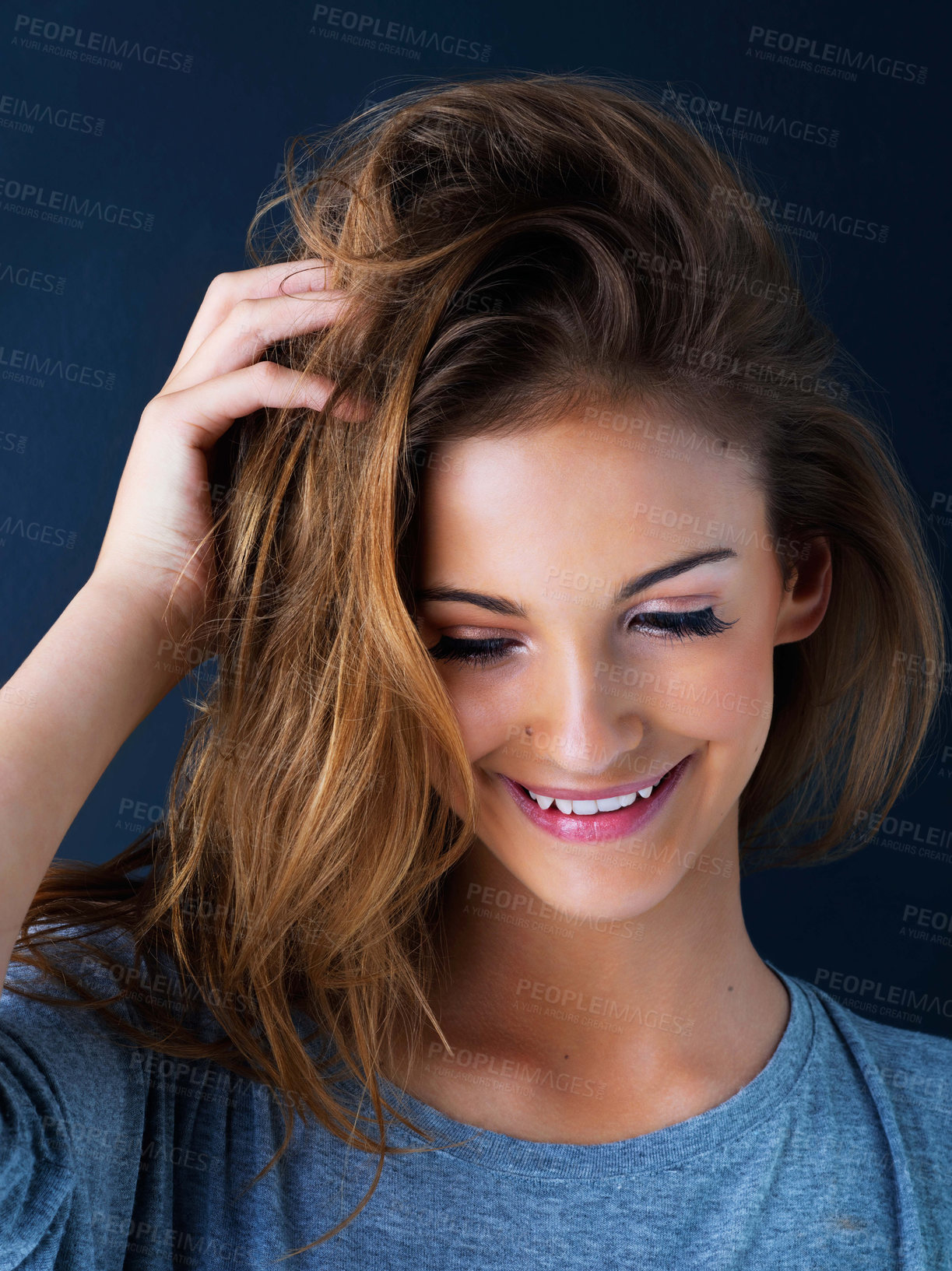 Buy stock photo Studio shot of a cute teenage girl with her hand in her hair posing against a dark background