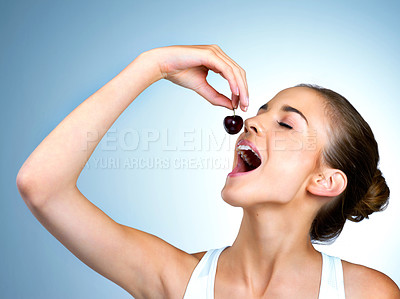 Buy stock photo Shot of a health-conscious young woman eating a cherry in  studio