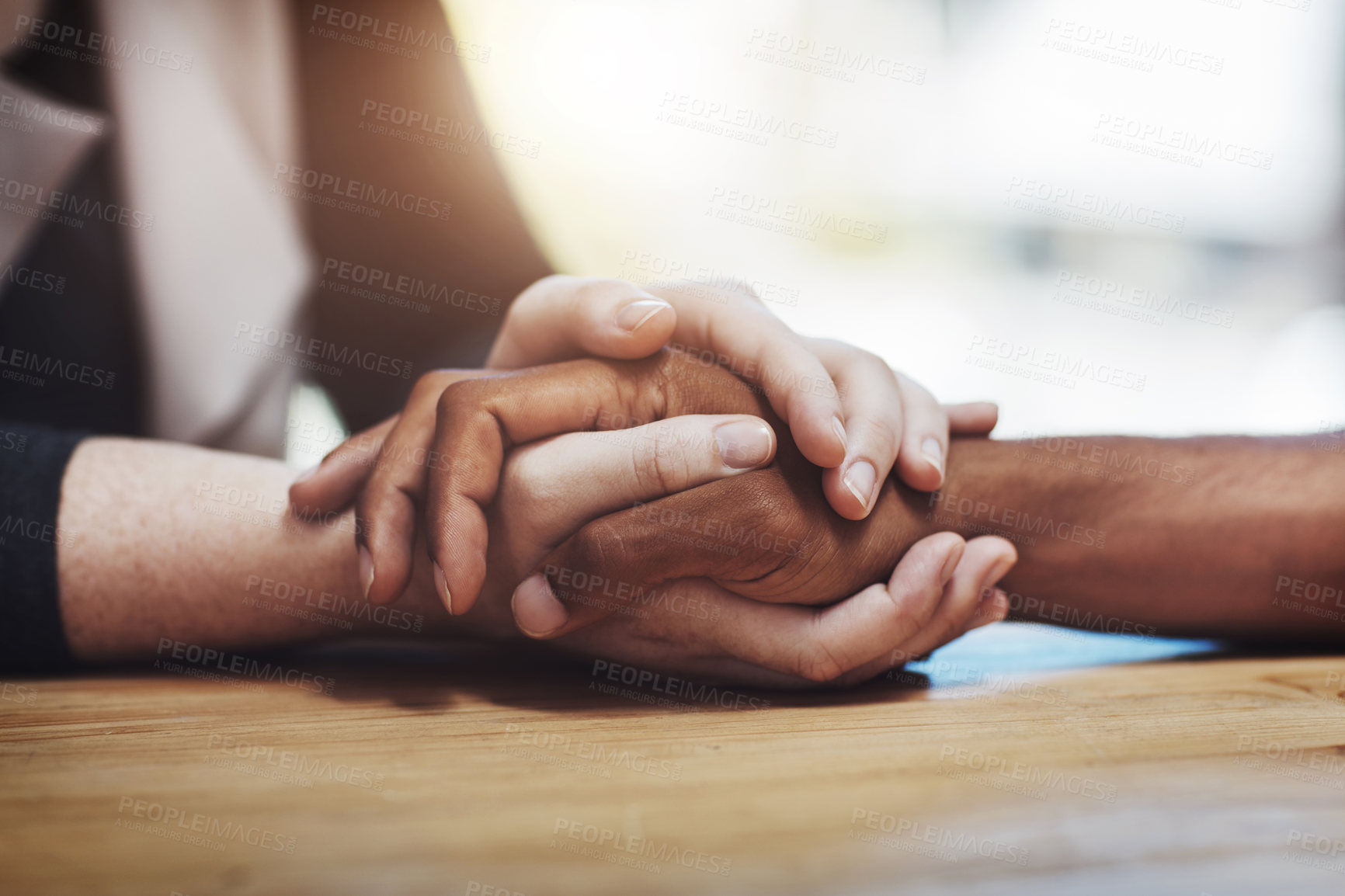 Buy stock photo Support, compassion and trust while holding hands and sitting together at a table. Closeup of a loving, caring and interracial couple or friends comforting each other after a loss or cancer news