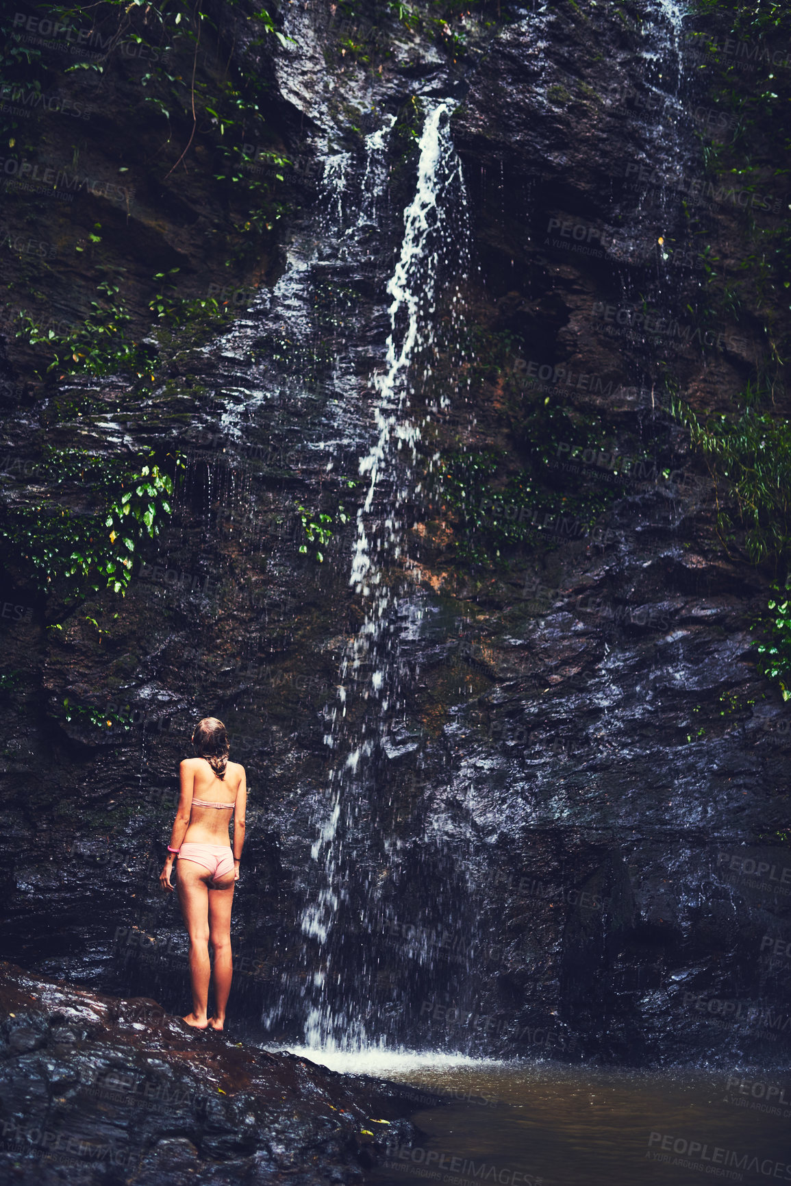 Buy stock photo Rearview shot of an unidentifiable young woman in a swimsuit admiring a waterfall in the jungle