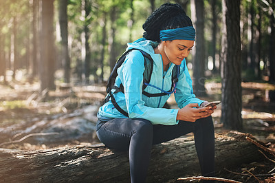 Buy stock photo Cropped shot of an athletic young woman sending a text while jogging in the woods