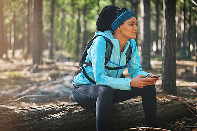 Buy stock photo Cropped shot of an athletic young woman sending a text while jogging in the woods