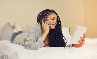 Buy stock photo Shot of a young woman talking on her phone while looking at something on her tablet