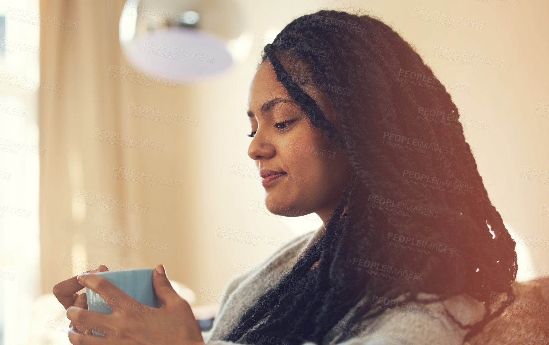 Buy stock photo Shot of a young woman enjoying a cup of coffee in her living room