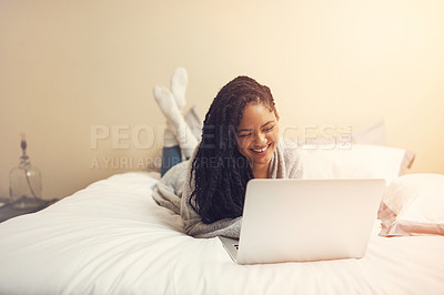 Buy stock photo Shot of a young woman using her laptop while lying in her bedroom