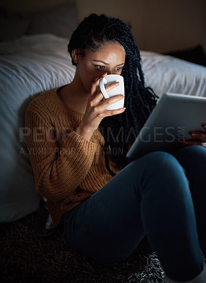 Buy stock photo Shot of a relaxed young woman drinking coffee and using a digital tablet during the evening at home