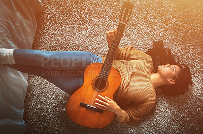Buy stock photo Shot of a relaxed young woman lying on the floor and playing an acoustic guitar at home
