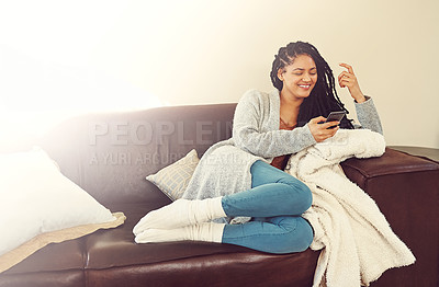 Buy stock photo Shot of a young woman using her phone while relaxing in her her living room