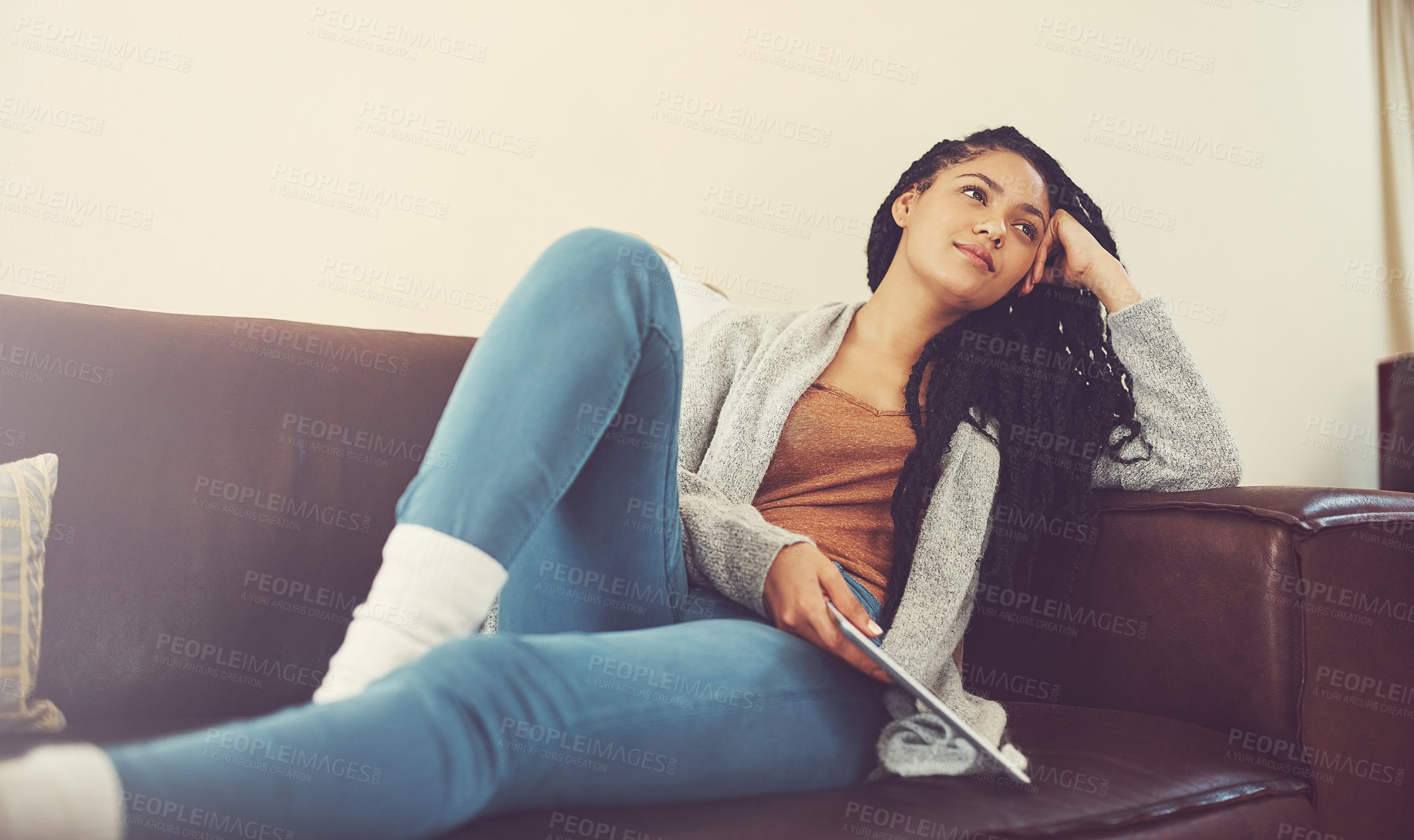 Buy stock photo Shot of a young woman contemplating while relaxing at home with her tablet