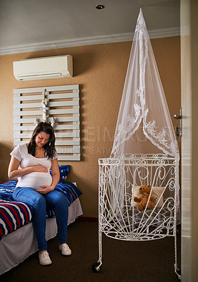 Buy stock photo Shot of a pregnant woman cradling her belly while sitting in the nursery at home