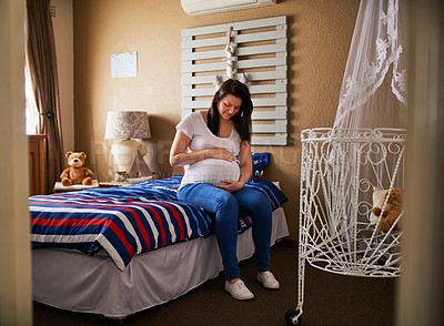 Buy stock photo Shot of a pregnant woman cradling her belly while sitting in the nursery at home