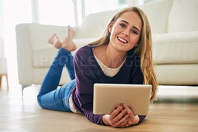 Buy stock photo Portrait of an attractive young woman using her tablet while lying on the floor at home