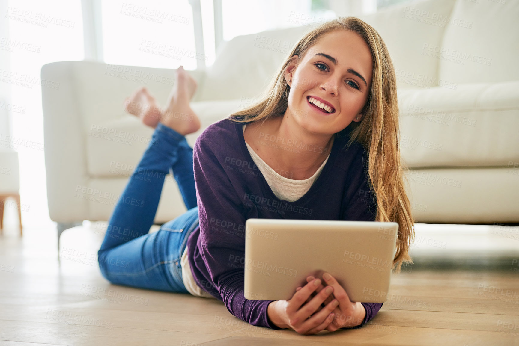 Buy stock photo Portrait of an attractive young woman using her tablet while lying on the floor at home