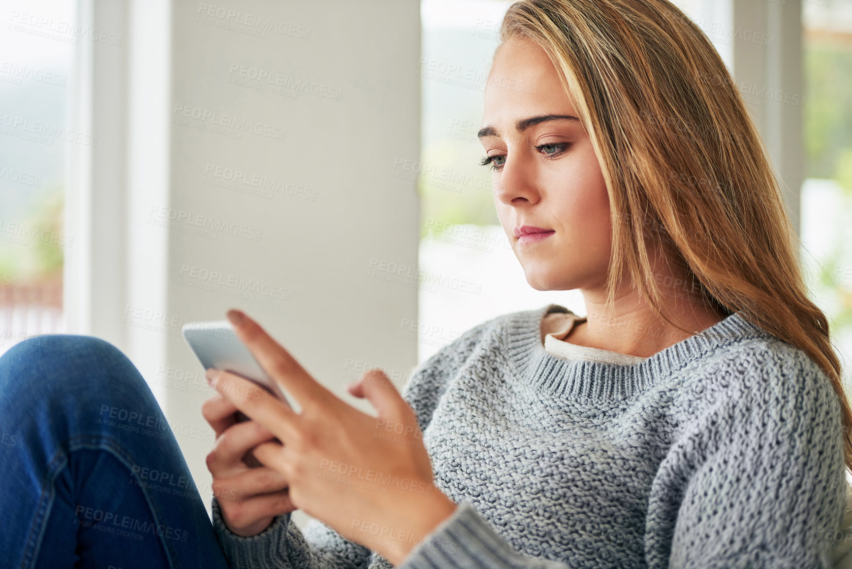 Buy stock photo Cropped shot of an attractive young woman sending a text message while chilling at home