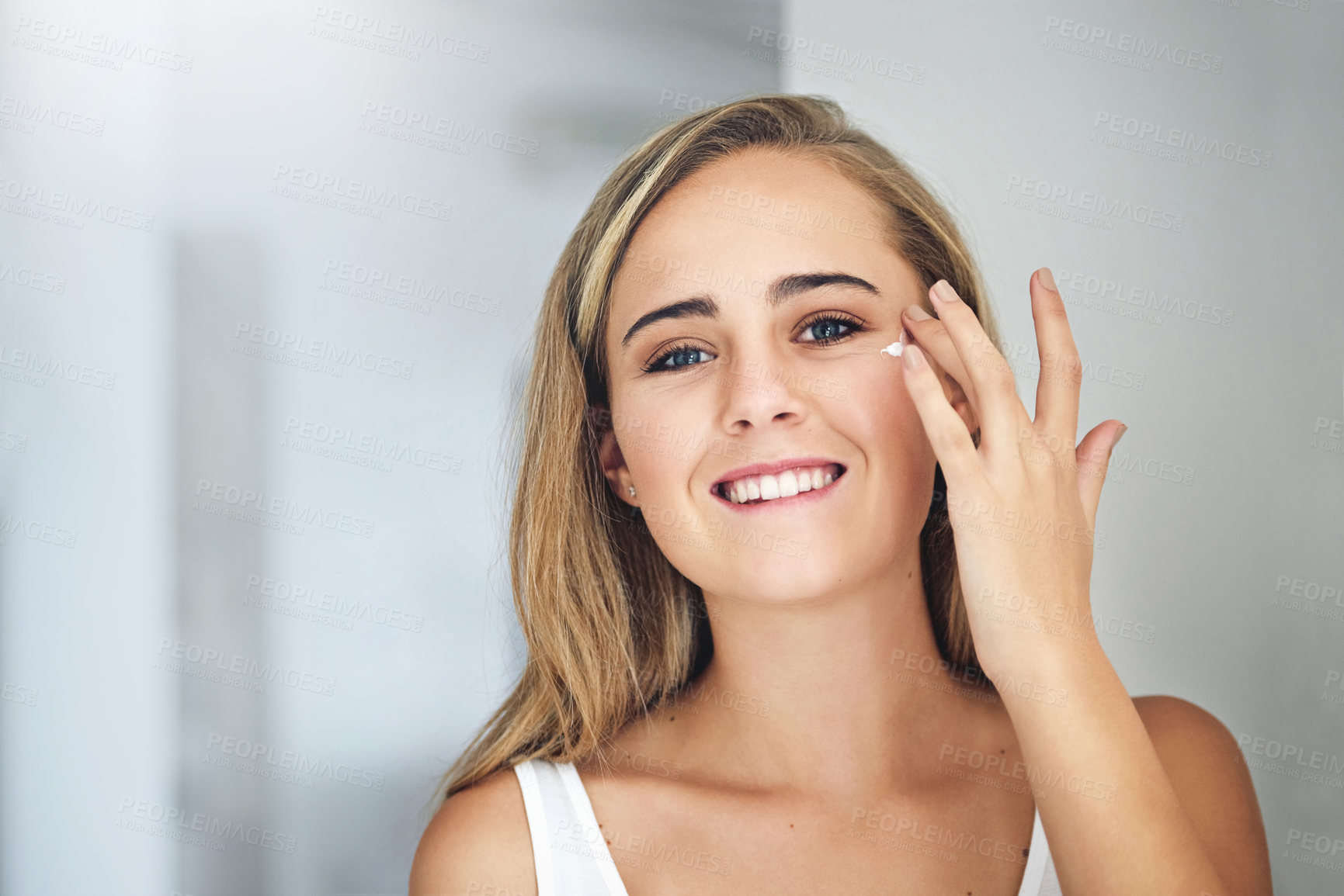 Buy stock photo Cropped shot of an attractive young woman applying moisturizer to her face in the bathroom