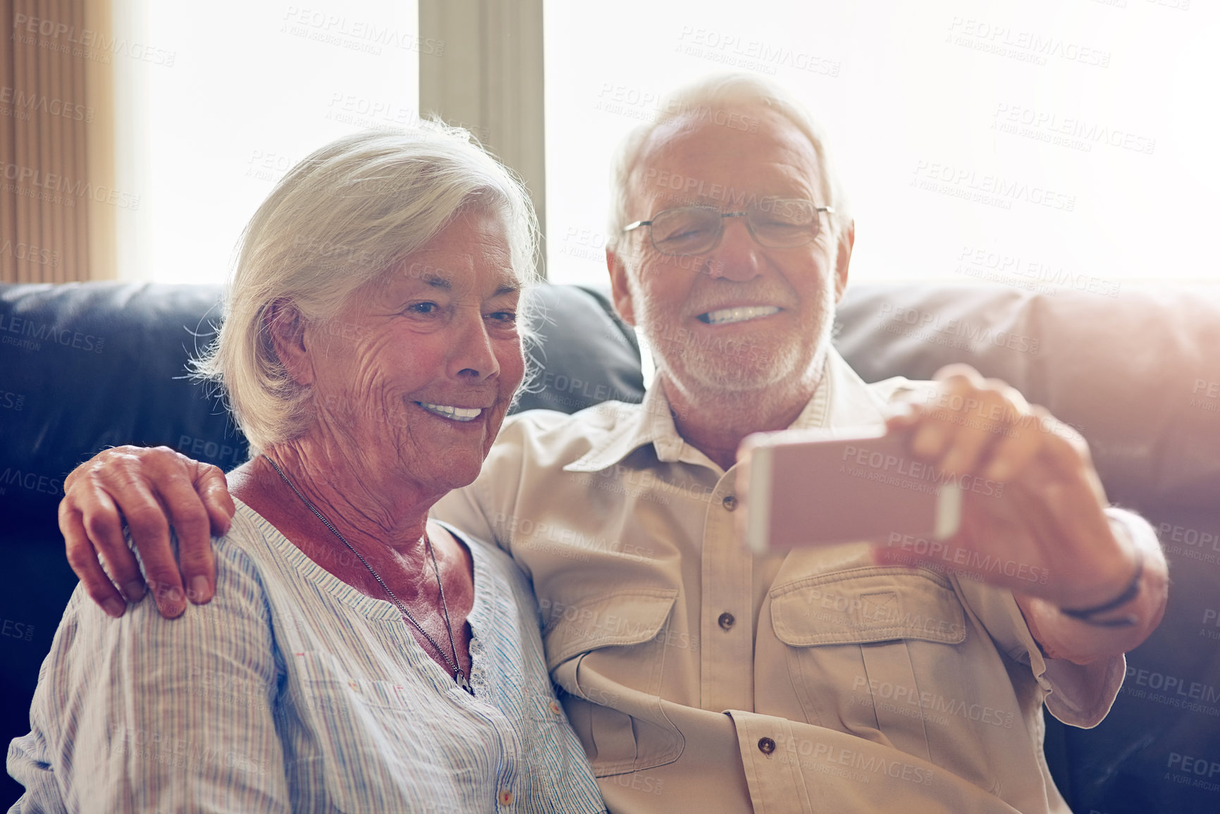 Buy stock photo Shot of a happy senior couple taking a selfie together on the sofa at home