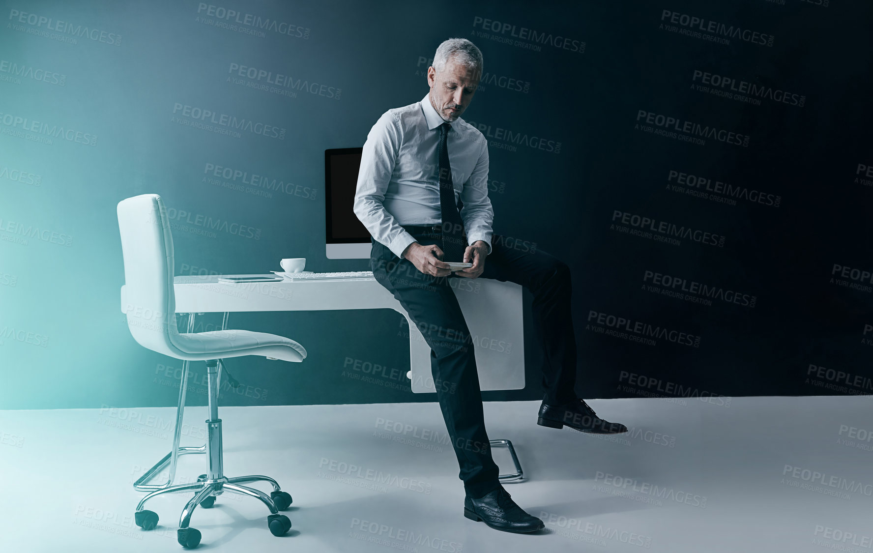 Buy stock photo Shot of a focussed businessman using his smartphone while sitting on his desk in the office