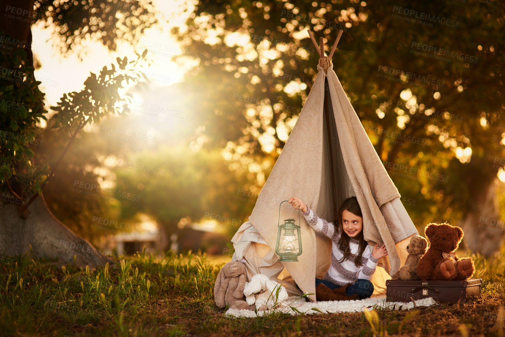 Buy stock photo Teepee, child and fun in garden tent outdoor in nature for camping, playing and adventure with sunlight. Cloth, lamp and fantasy house for girl in forest with imagination, suitcase and teddy bear