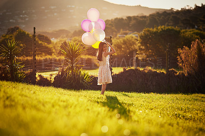Buy stock photo Portrait of a cute little girl holding a big bunch of balloons while walking outside